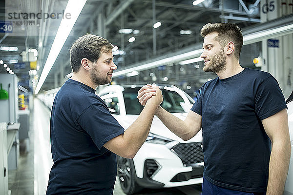 Zwei Kollegen schütteln sich in moderner Autofabrik die Hand