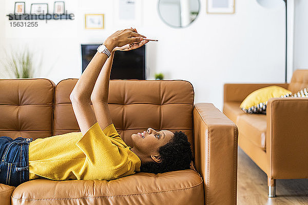 Junge Frau liegt zu Hause auf dem Sofa und benutzt ein Smartphone