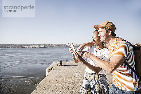 Junges Paar telefoniert mit seinem Handy am Pier am Wasser  Lissabon  Portugal