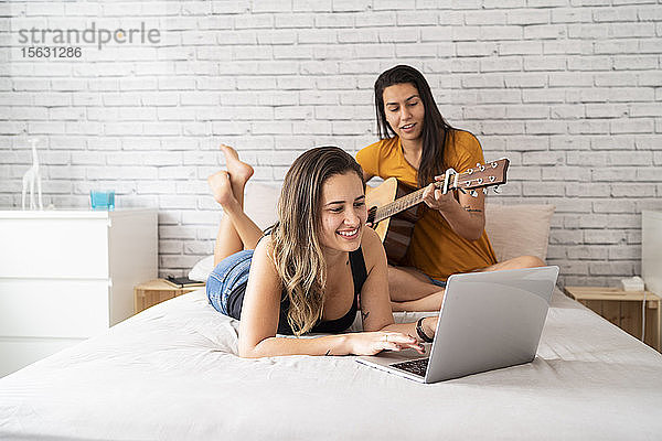 Glückliches lesbisches Paar mit Laptop und Gitarre im Bett