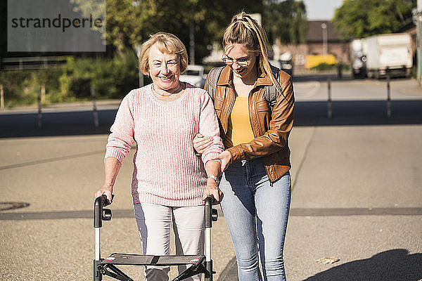 Enkelin hilft ihrer Großmutter beim Laufen mit einer Gehhilfe auf Rädern