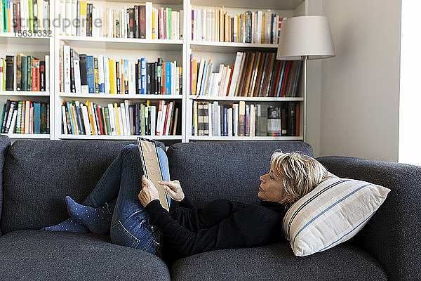 Reife Frau entspannt zu Hause auf der Couch mit Grafiktablett