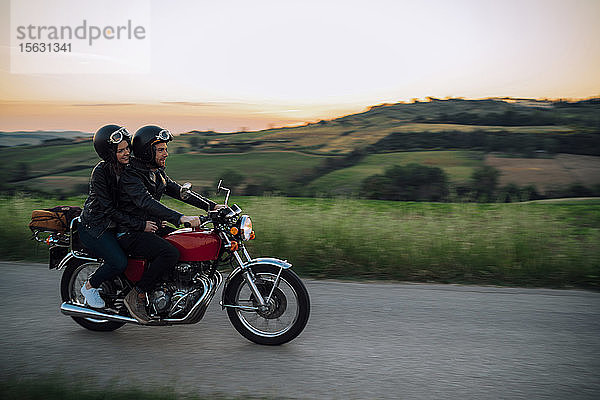 Junges Paar mit einem Oldtimer-Motorrad auf einer Landstraße bei Sonnenuntergang  Toskana  Italien