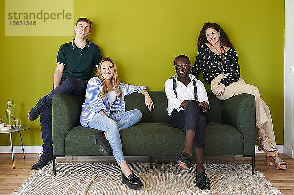 Porträt von lächelnden Kollegen  die in einer grün ummauerten Bürolounge auf einem Sofa sitzen