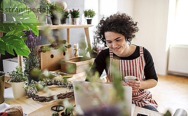 Lächelnde junge Frau mit Laptop in einem kleinen Laden mit Pflanzen