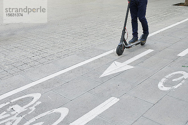 Beine eines Mannes  der auf einem E-Scooter auf dem Fahrradweg in der Stadt fährt