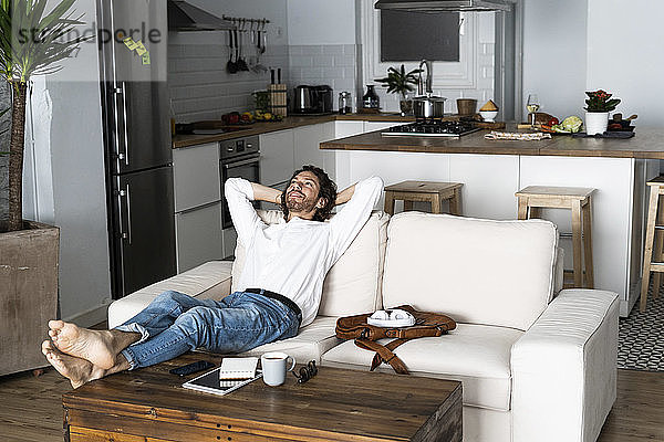 Entspannter Mann lehnt sich zu Hause auf dem Sofa zurück