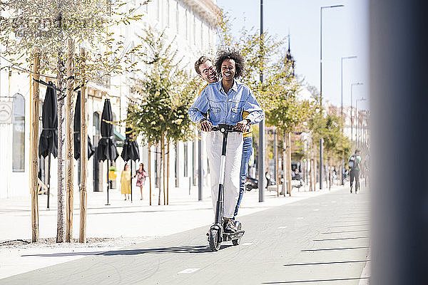 Glückliches junges Paar fährt E-Scooter in der Stadt