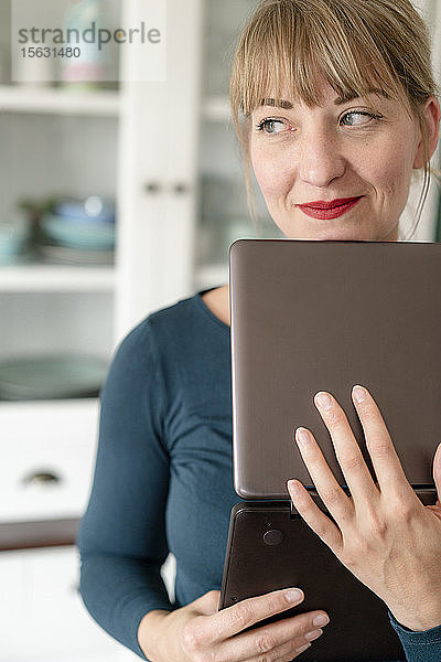 Porträt einer lächelnden Frau mit Laptop in der Küche  die in die Ferne schaut