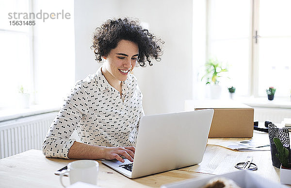 Lächelnde junge Frau arbeitet am Laptop am Schreibtisch