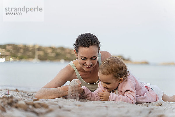 Glückliche Mutter und Tochter spielen mit Sand am Strand