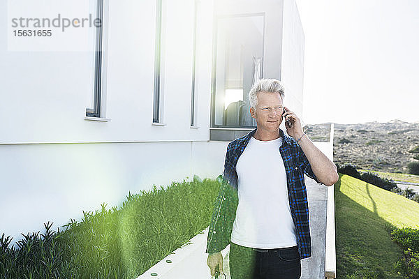 Lässiger Mann vor seinem modernen Zuhause beim Telefonieren