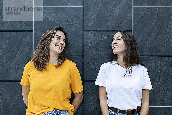 Zwei Freunde  die sich an eine graue Wand lehnen und lachen