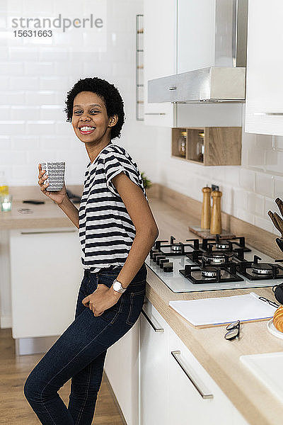 Porträt einer lächelnden jungen Frau  die zu Hause in der Küche einen Becher hält