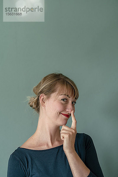 Porträt einer lächelnden Frau  die ihre Nasenspitze berührt