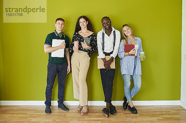 Porträt von lächelnden Gelegenheitskollegen  die zusammen vor einer grünen Wand in einem modernen Büro stehen
