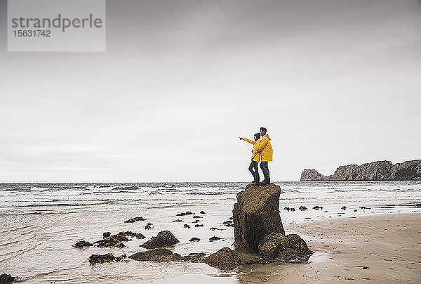 Junge Frau in gelben Regenjacken und auf einem Felsen am Strand stehend  Bretagne  Frankreich