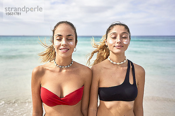 Zwei junge Frauen stehen mit geschlossenen Augen am Strand