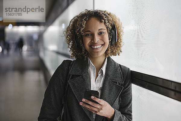 Porträt einer lächelnden Frau mit Kopfhörer und Smartphone