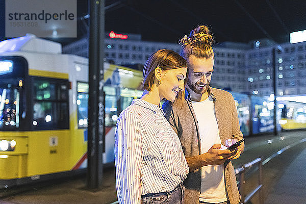 Glückliches Paar in der Stadt  das nachts sein Telefon kontrolliert  Berlin  Gernany