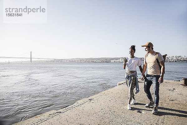 Junges Paar mit Handy auf dem Pier am Wasser  Lissabon  Portugal