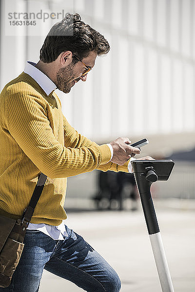 Junger Mann mit E-Scooter benutzt Handy in der Stadt