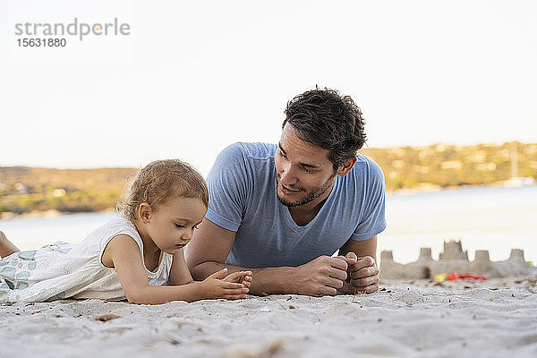 Vater und Tochter am Strand liegend