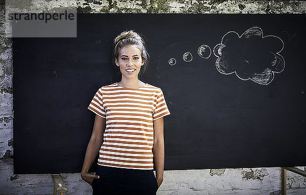 Lächelnde junge Frau steht vor einer Tafel neben einer Gedankenblase