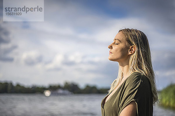 Frau mit geschlossenen Augen an einem See stehend