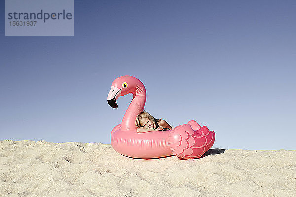 Lächelndes Mädchen liegt auf einem Flamingo-Poolwagen und schaut in die Kamera
