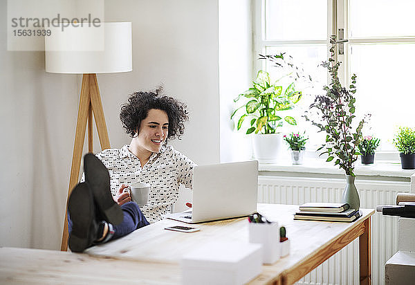 Entspannte junge Frau arbeitet am Schreibtisch am Laptop