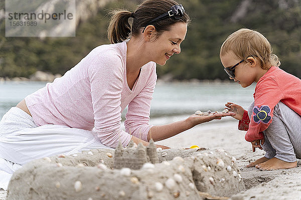 Glückliche Mutter und Tochter bauen eine Sandburg am Strand