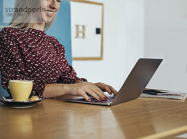 Frau  die in einem Café Kaffee trinkt und auf ihren Laptop schaut
