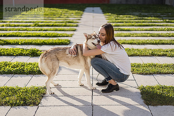 Glückliche junge Frau kuschelt mit ihrem Hund im Freien