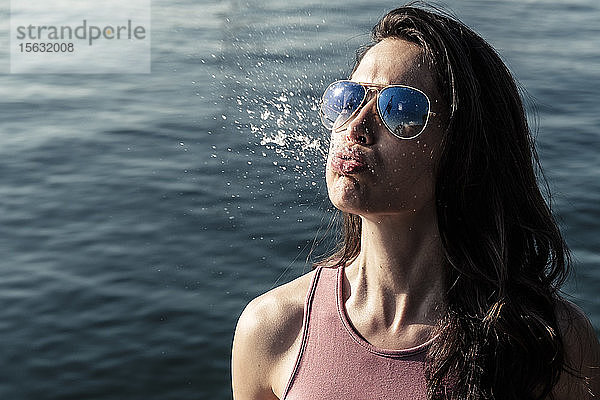 Porträt einer jungen Frau mit Sonnenbrille  die Wasser schnauft