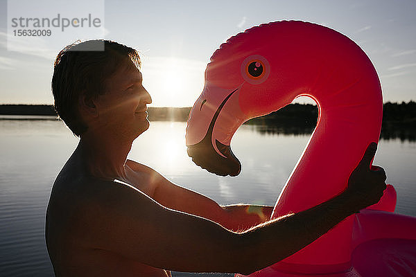 Junger Mann mit Flamingo-Pool schwebt bei Sonnenuntergang