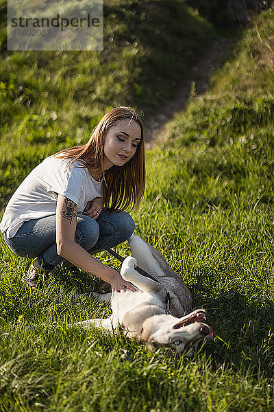 Porträt einer jungen Frau  die ihren Hund auf einer Wiese streichelt