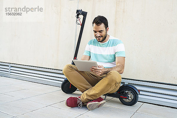Porträt eines auf einem Elektroroller sitzenden Mannes mit digitalem Tablet
