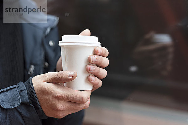 Junger Mann hält einen Kaffee zum Mitnehmen im Freien