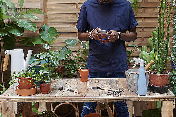 Junger Mann benutzt Smartphone auf seiner Terrasse bei der Gartenarbeit