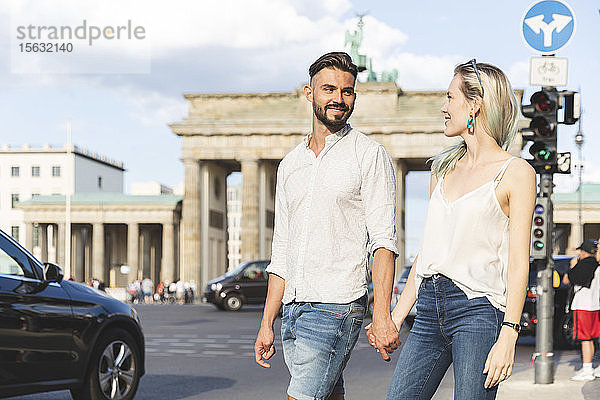 Glückliches junges Paar geht Hand in Hand vor dem Brandenburger Tor  Berlin  Deutschland