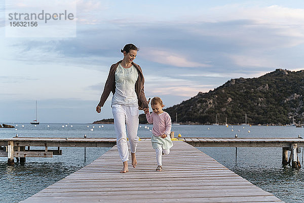 Glückliche Mutter mit Tochter geht bei Sonnenuntergang auf einem Steg spazieren