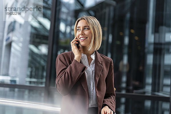 Lächelnde junge Geschäftsfrau am Telefon in der Stadt