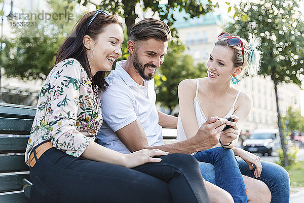 Drei Freunde sitzen zusammen auf einer Bank und schauen auf ihr Handy
