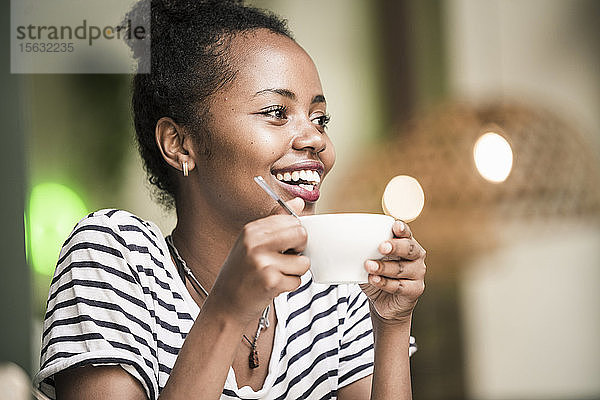 Porträt einer glücklichen jungen Frau  die in einem Café eine Kaffeetasse hält