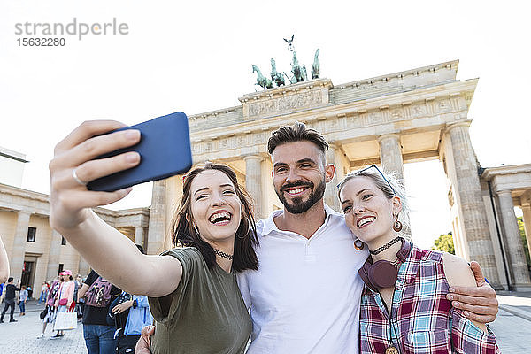 Porträt von drei glücklichen Freunden  die sich mit dem Handy vor dem Brandenburger Tor in Berlin selbstständig machen