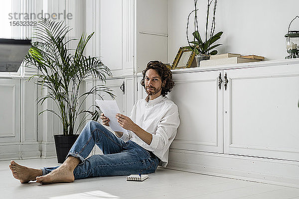 Porträt eines Mannes  der zu Hause auf dem Boden sitzt und Papiere durchsieht