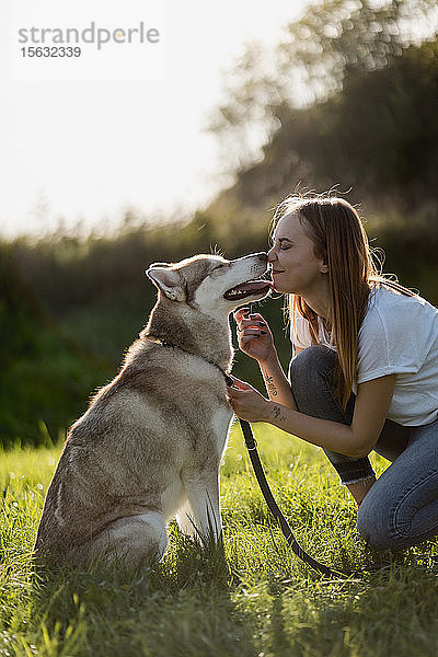 Junge Frau Nase an Nase mit ihrem Hund auf einer Wiese