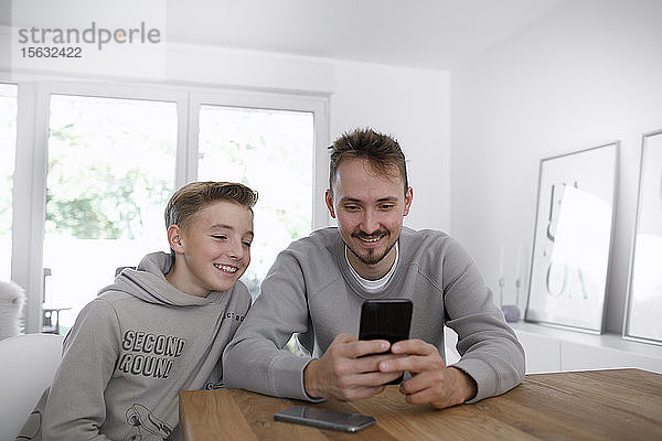 Junger Mann und Teenager benutzen ein Smartphone im Wohnzimmer