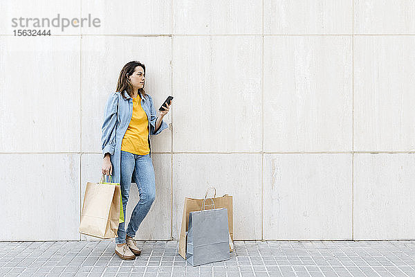 Junge brünette Frau benutzt Smartphone nach dem Einkauf